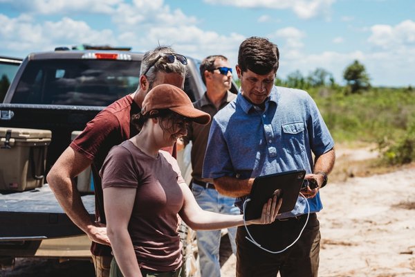 a group of people are standing in front of a truck looking at a tablet .