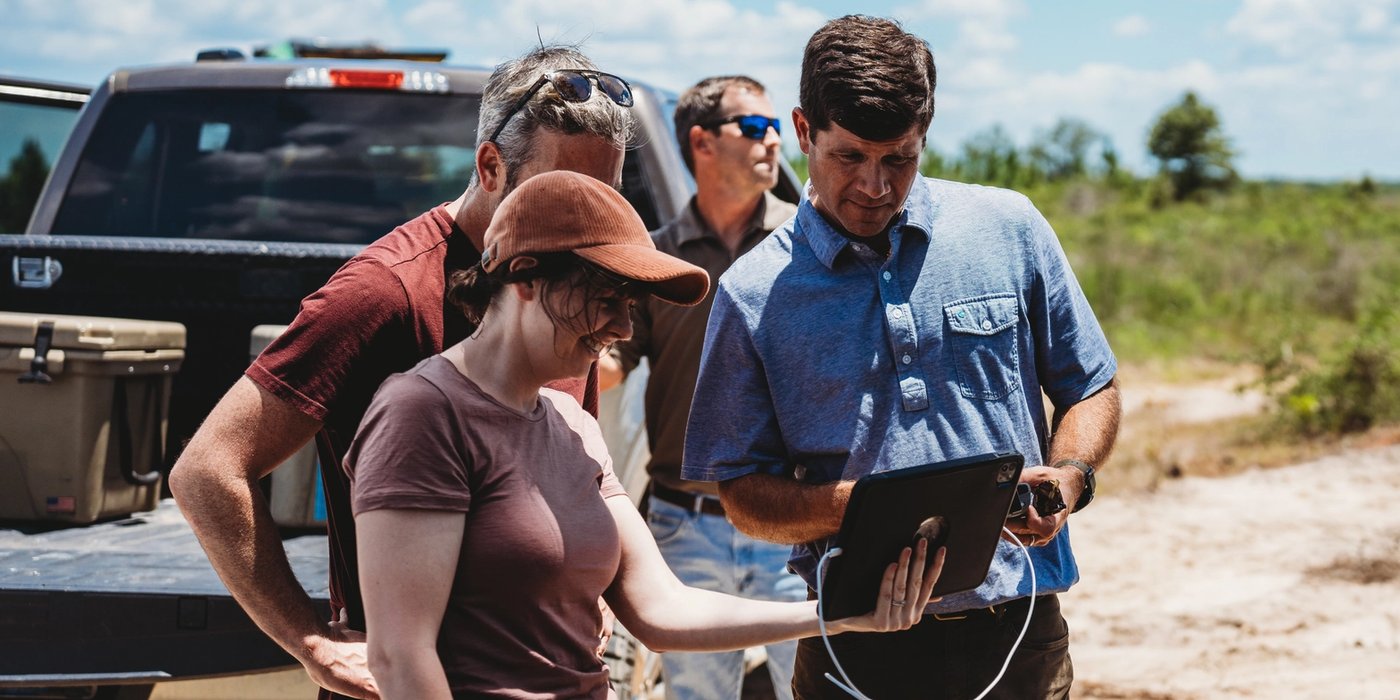a group of people are standing in front of a truck looking at a tablet .