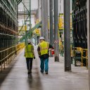 a man and a woman in safety vests and hard hats are walking beside a lumber sorter at a Canfor sawmill..
