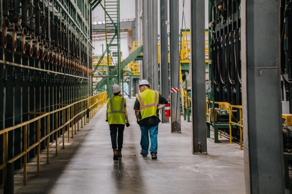 a man and a woman in safety vests and hard hats are walking beside a lumber sorter at a Canfor sawmill..