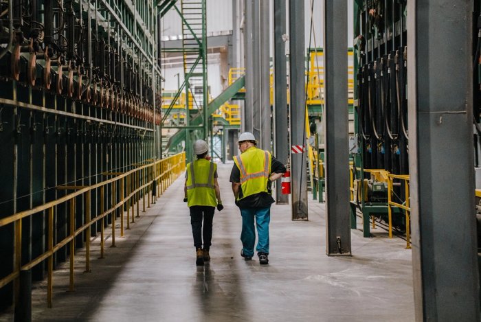 a man and a woman in safety vests and hard hats are walking beside a lumber sorter at a Canfor sawmill..