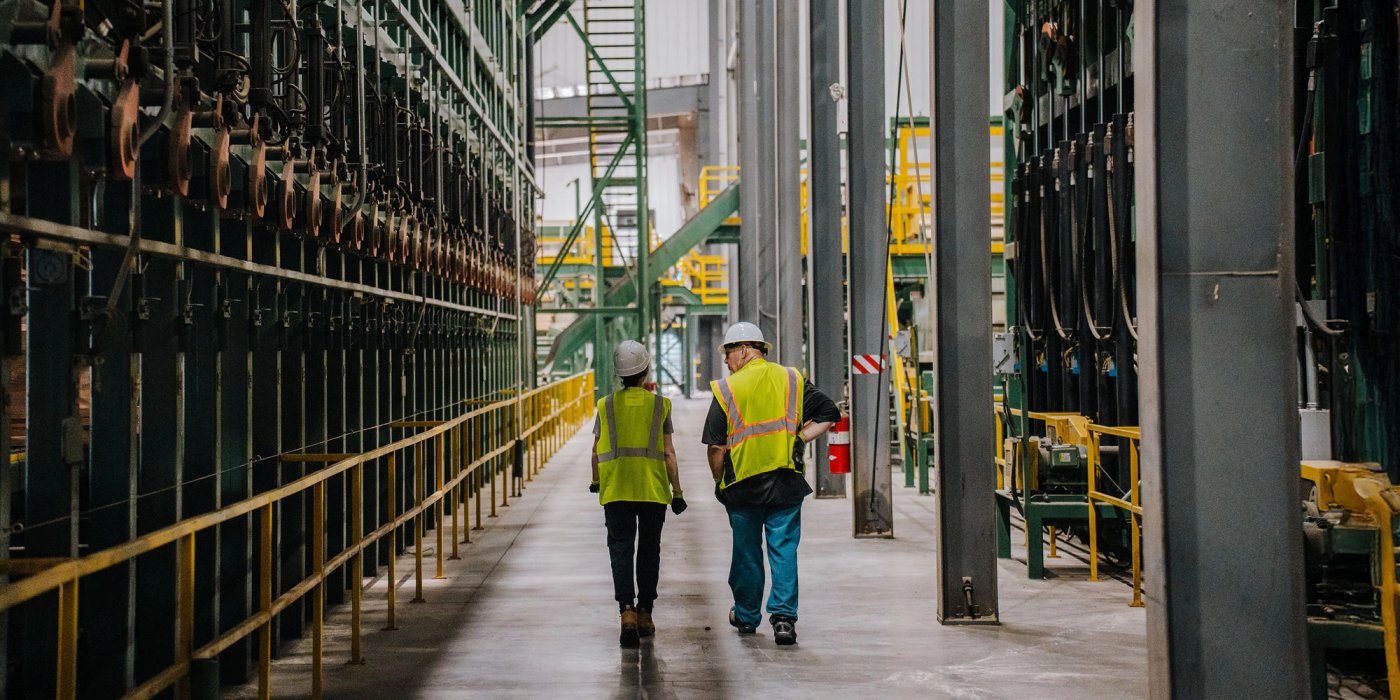 a man and a woman in safety vests and hard hats are walking beside a lumber sorter at a Canfor sawmill..