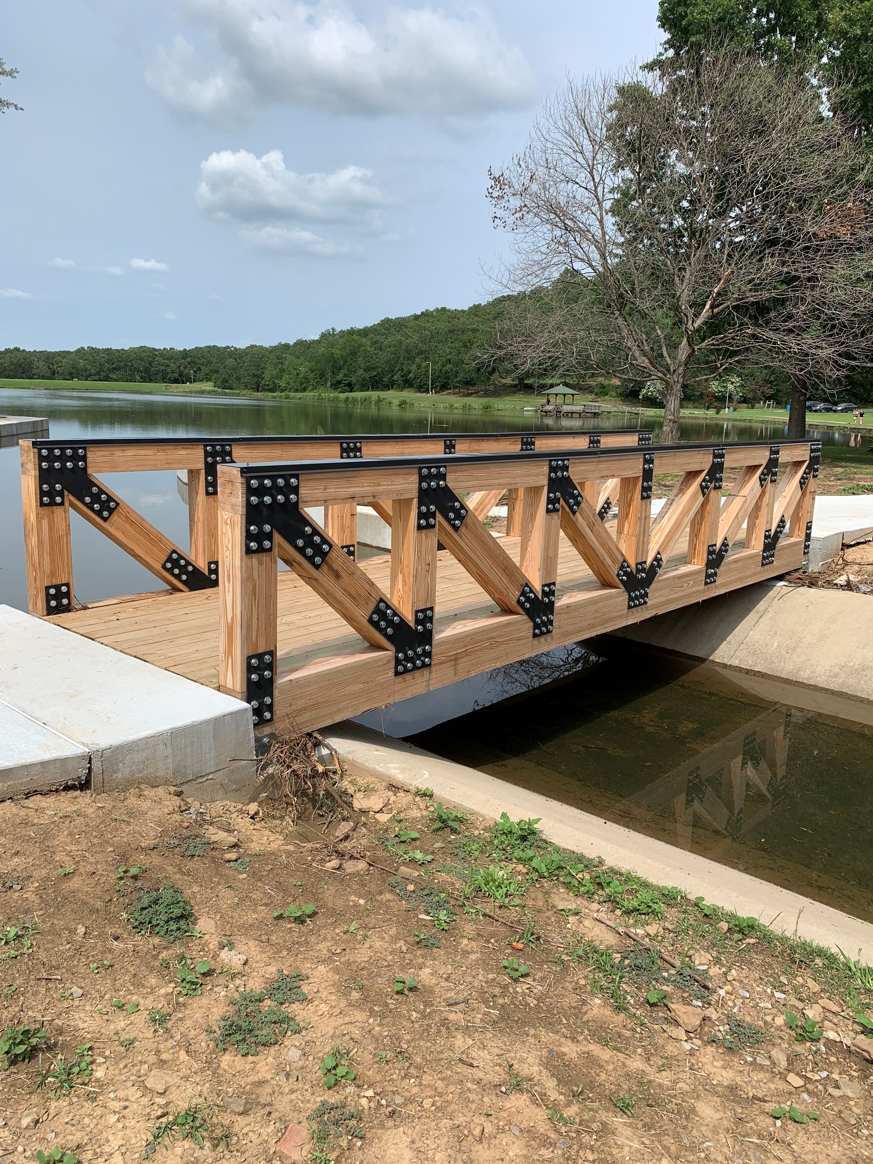 a wooden bridge over a body of water with trees in the background.