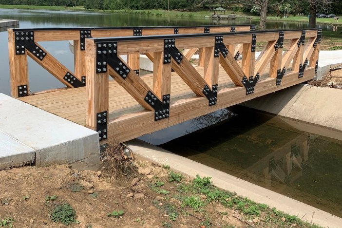 a wooden bridge over a body of water with trees in the background.