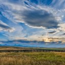 a field with a fence in the foreground and a cloudy sky in the background .