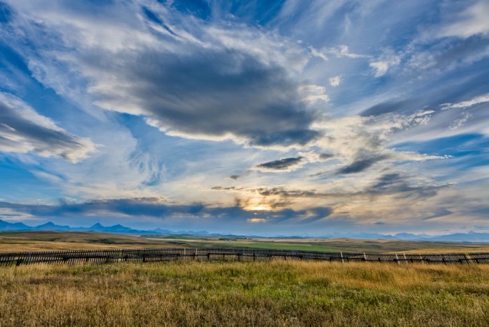 a field with a fence in the foreground and a cloudy sky in the background .
