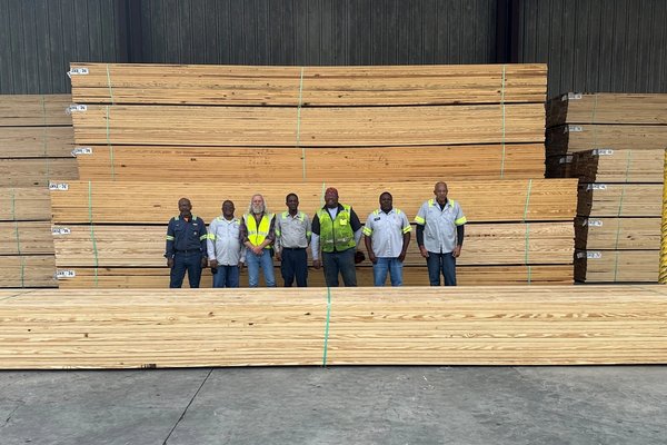 a group of men are standing in front of a large stack of wood .