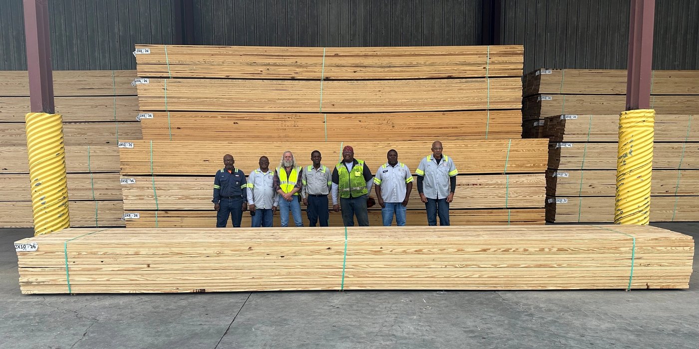a group of men are standing in front of a large stack of wood .