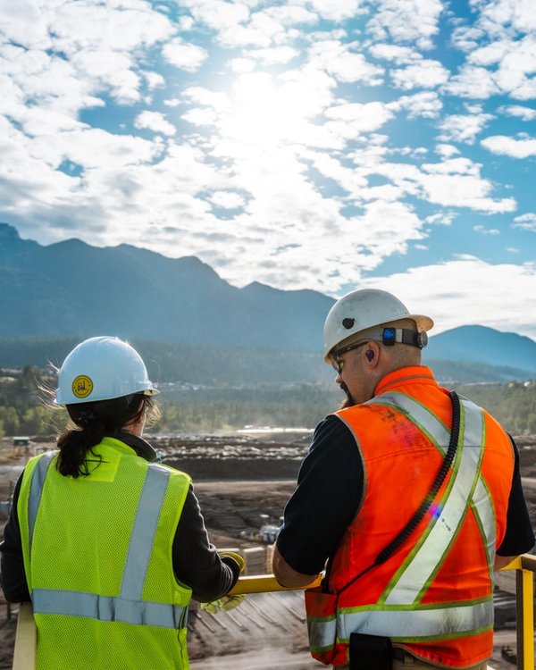 a man and a woman wearing hard hats and safety vests are looking out over a construction site .