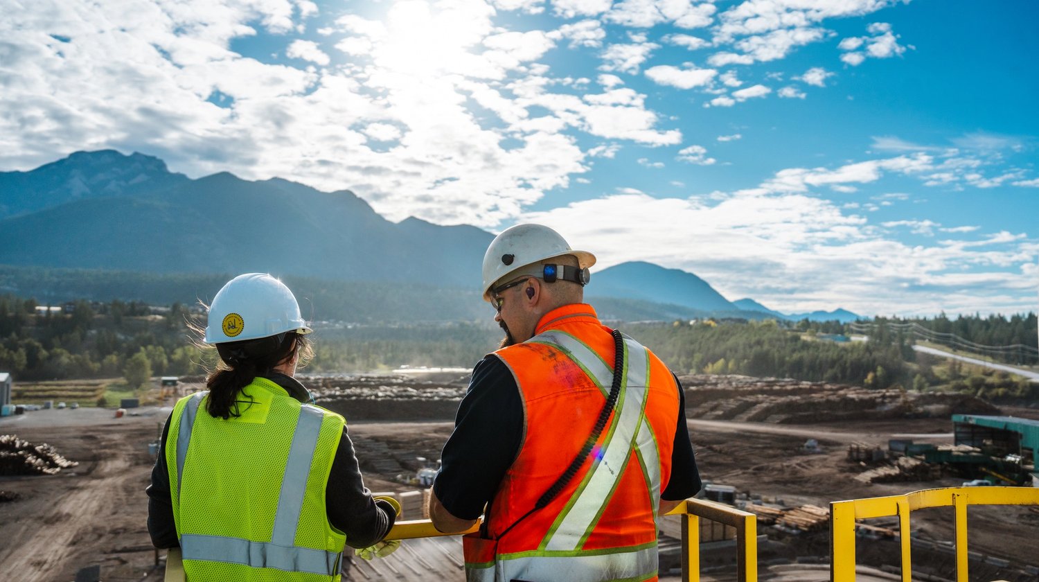 a man and a woman wearing hard hats and safety vests are looking out over a construction site .