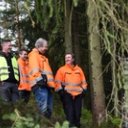 Five men in high-visibility jackets smiling and talking in a forest, next to a large yellow machine.