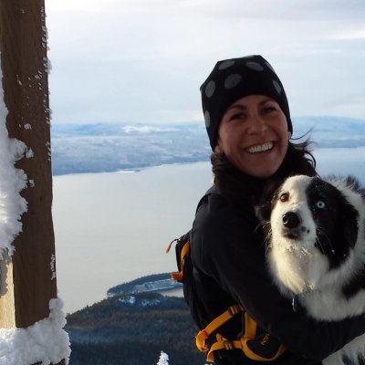 a woman is holding a black and white dog on top of a snow covered mountain .