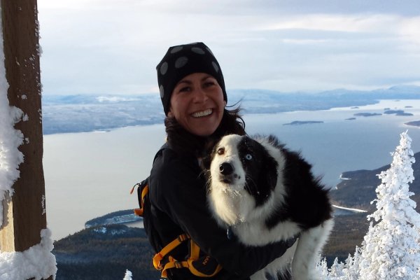 a woman is holding a black and white dog on top of a snow covered mountain .