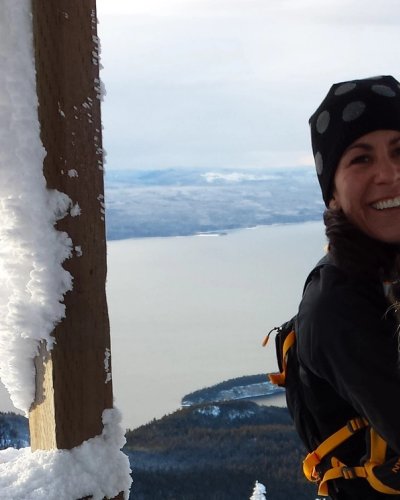 a woman is holding a black and white dog on top of a snow covered mountain .