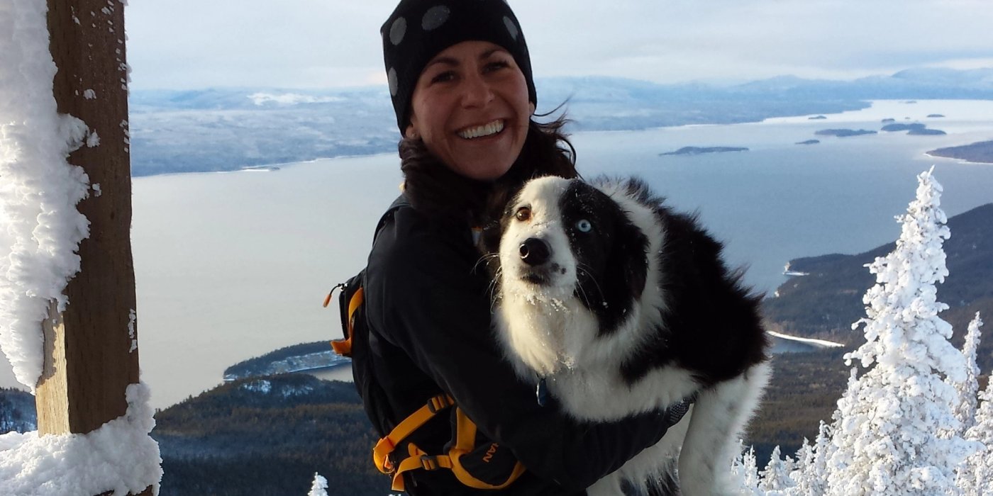 a woman is holding a black and white dog on top of a snow covered mountain .
