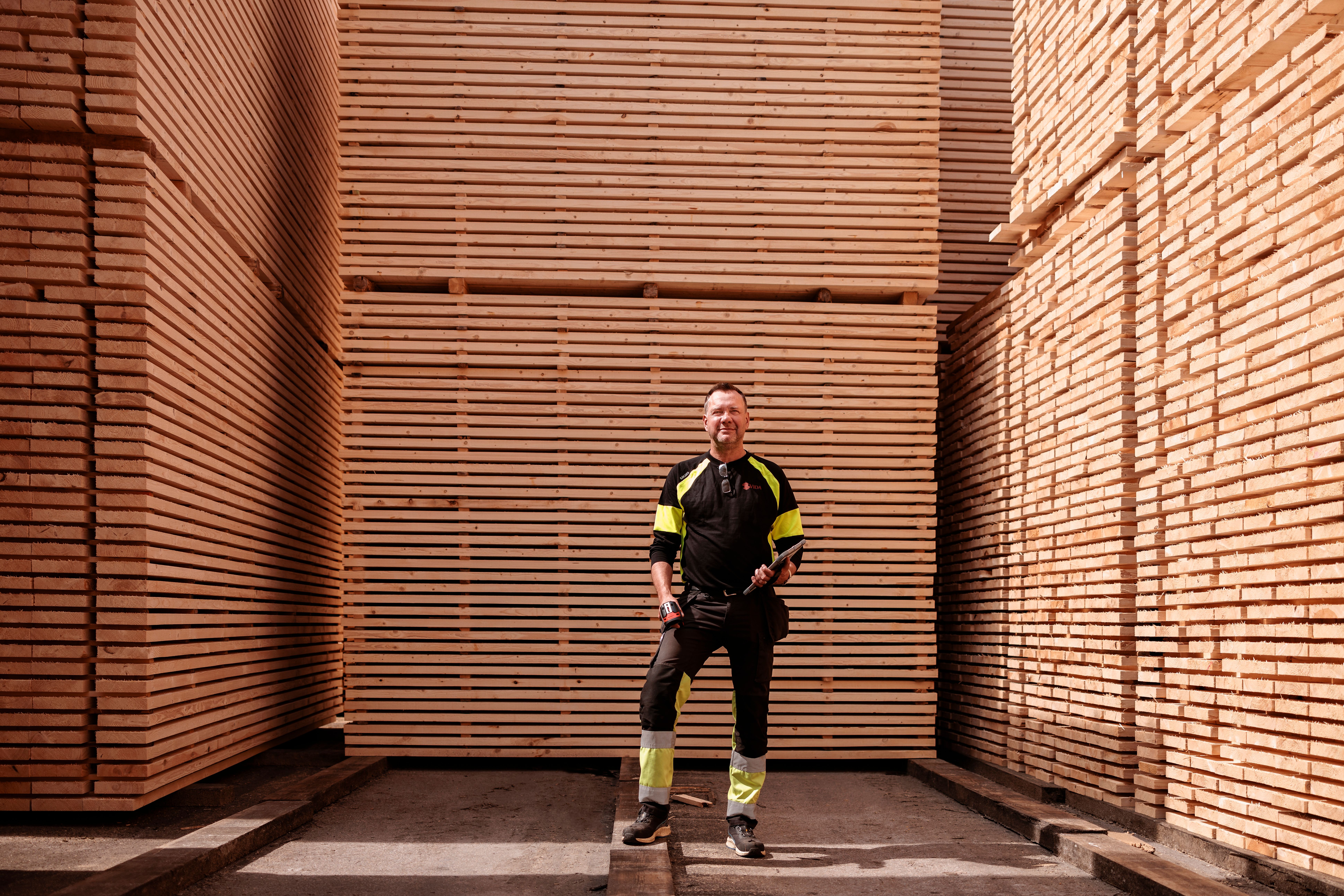 a man is standing in front of a large stack of lumber.