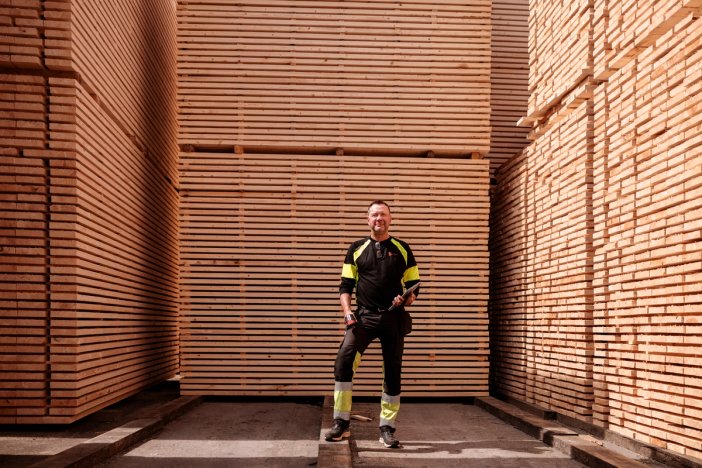 a man is standing in front of a large stack of lumber.