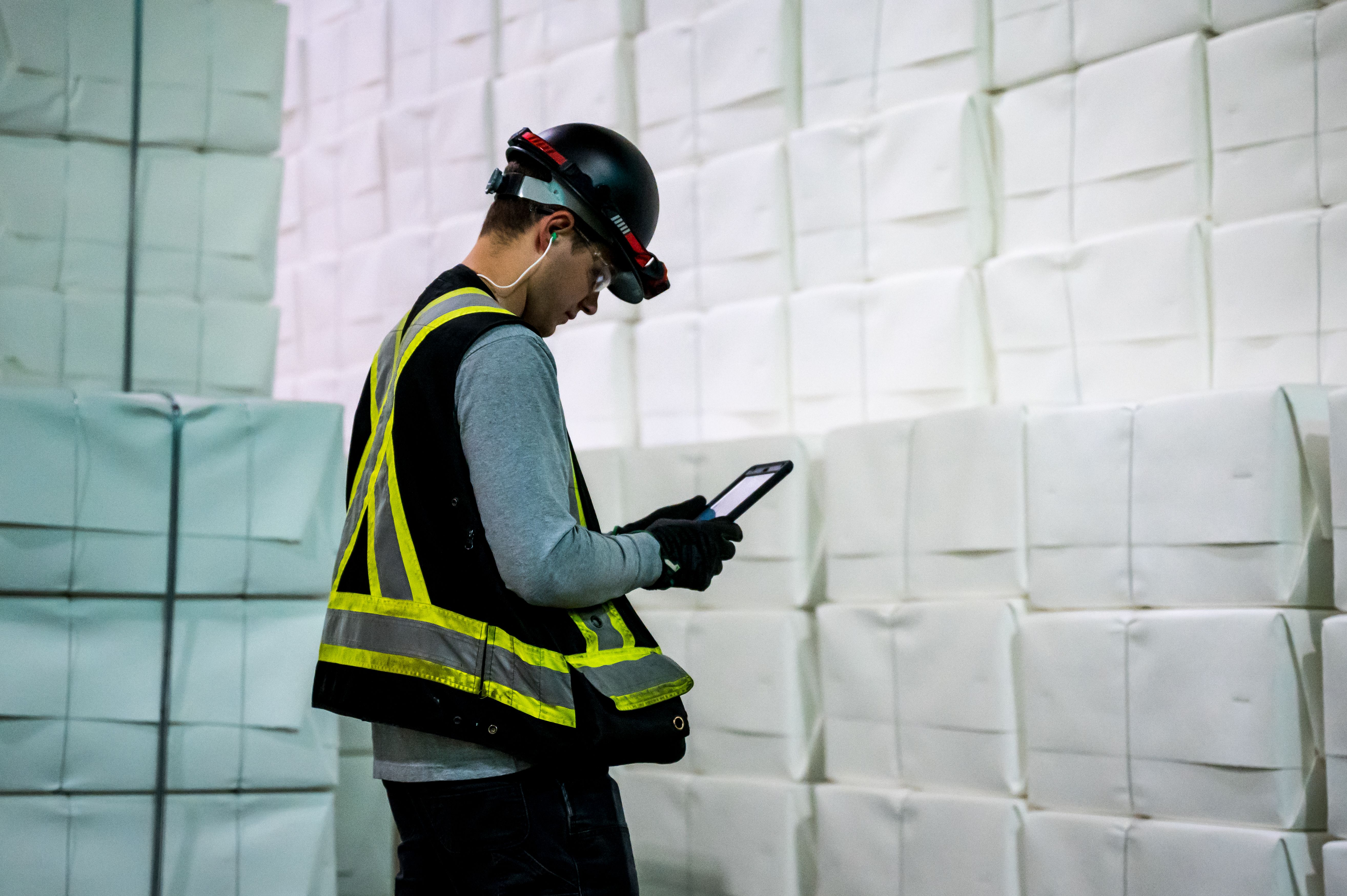a man wearing a hard hat and safety vest is using a tablet in a warehouse .
