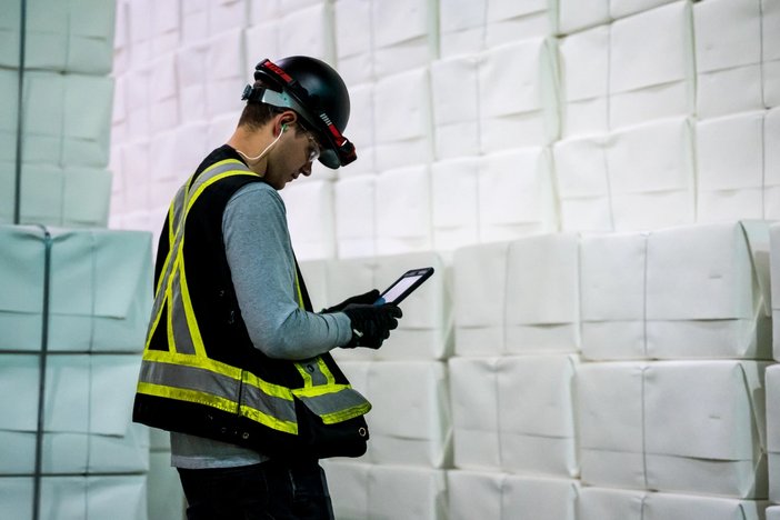 a man wearing a hard hat and safety vest is using a tablet in a warehouse .