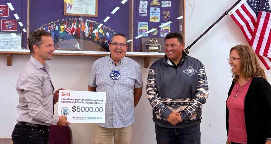 A man presents a large $5000 check for the Shuswap Band Cultural and Family Wellness Centre to another man, as two others smile beside them.