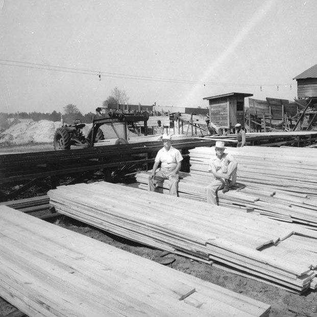 a black and white photo of two men sitting on a pile of wood
