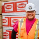 a man wearing a hard hat and safety vest is standing in front of a stack of Canfor lumber.