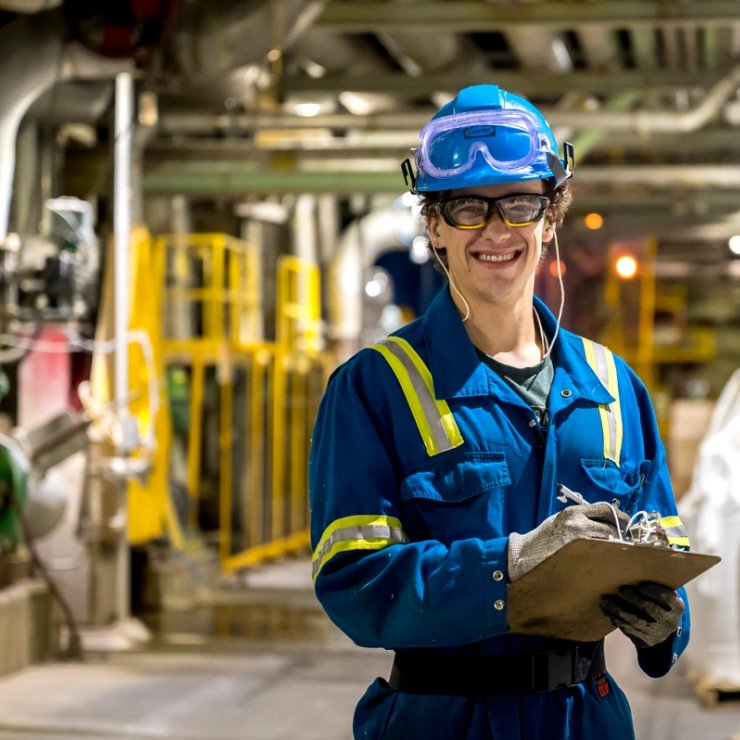 a man wearing a hard hat and goggles is holding a clipboard in a factory .