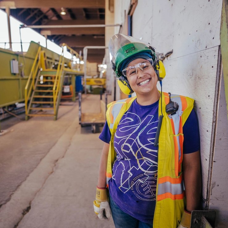 a woman wearing a hard hat and safety vest is standing in a factory .