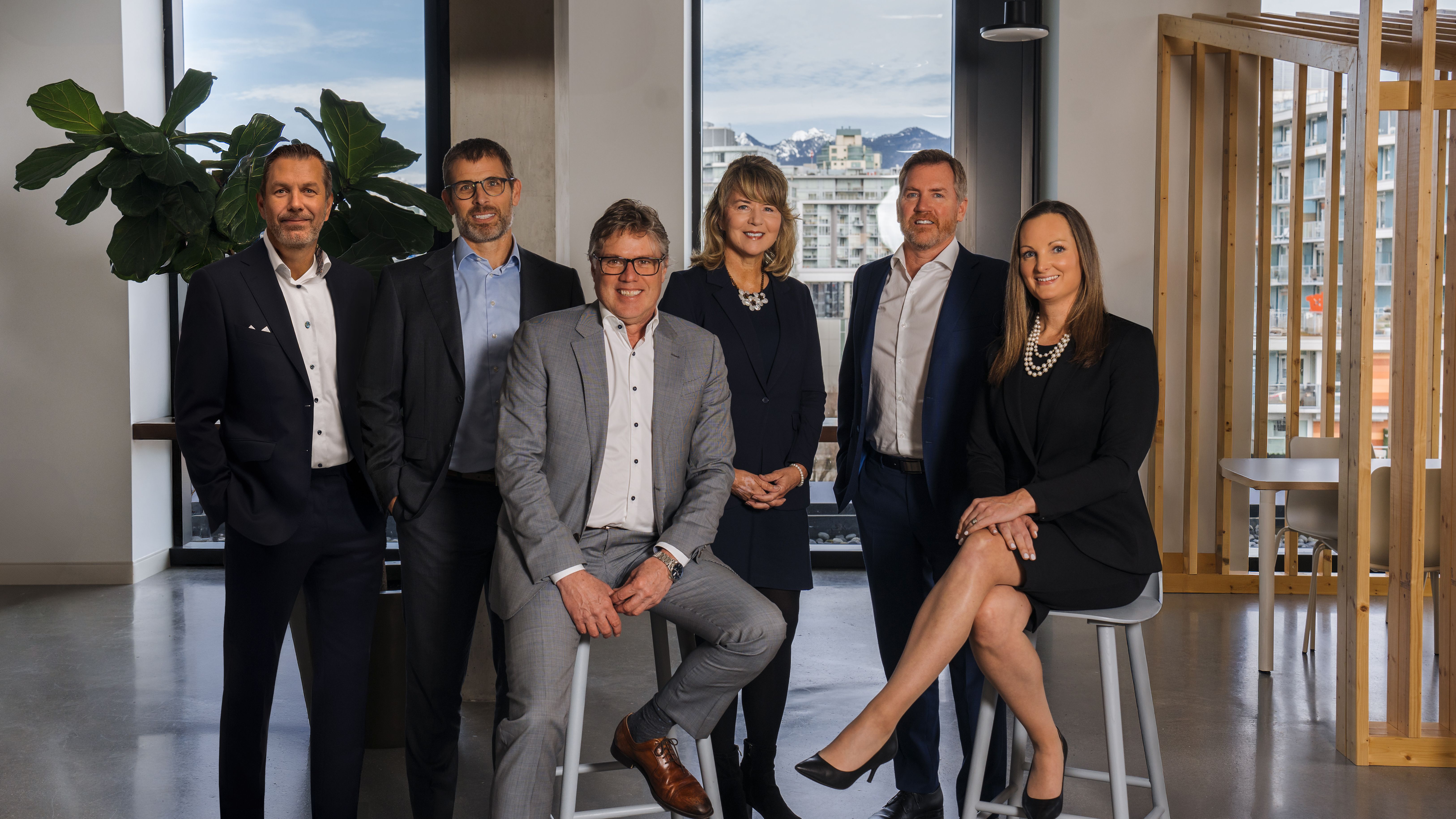 Six professionals in business attire in a modern office with city and mountain views.