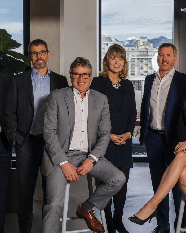 Six professionals in business attire in a modern office with city and mountain views.