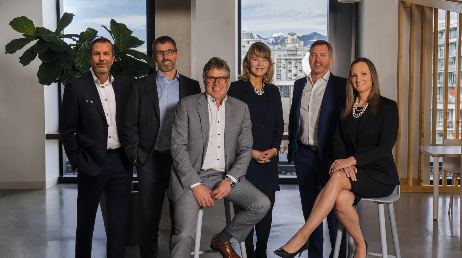 Six professionals in business attire in a modern office with city and mountain views.