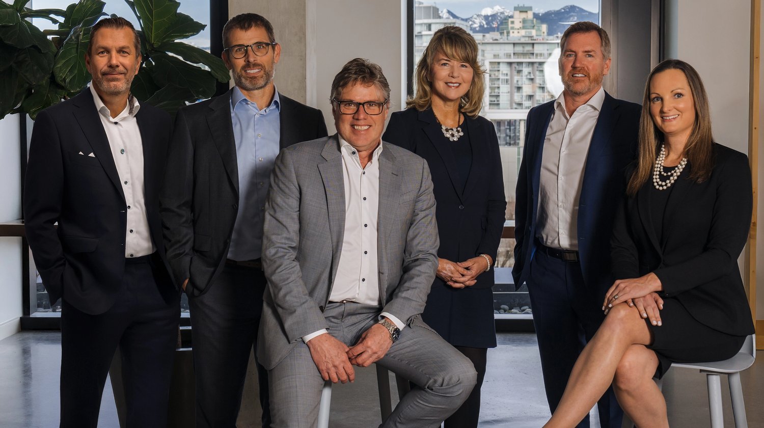 Six professionals in business attire in a modern office with city and mountain views.