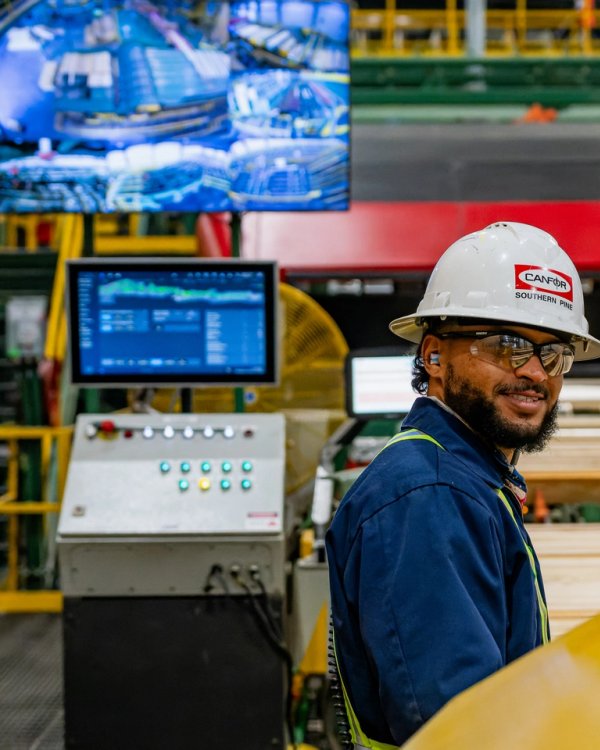 a man wearing a hard hat and safety vest is standing in a factory .