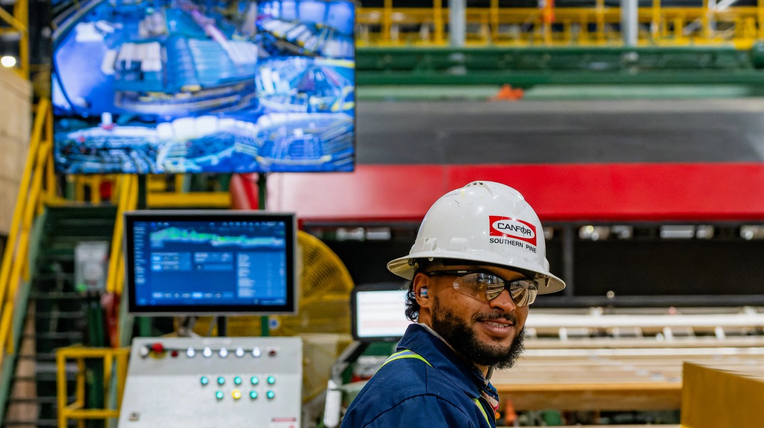 a man wearing a hard hat and safety vest is standing in a factory .