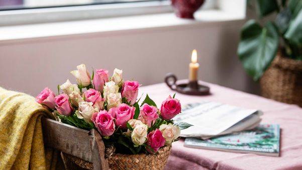 Rosa og hvite roser står på en stol foran et bord med rosa duk med stearinlys på