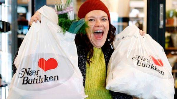 Smilende Nærbutikken-kunde holder opp to plastposer fra Nærbutikken