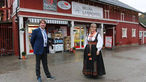Mann i dress og kvinne i bunad foran Nærbutikken på Hegra