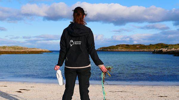 En kvinne står med plast-avfall i hendene og ser ut over havet