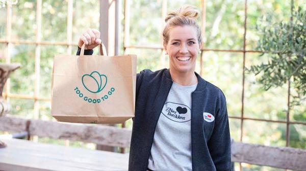 Smilende Nærbutikken ansatt holder en pose fra Too Good To Go