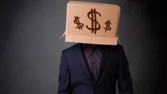 Young man standing and gesturing with a cardboard box on his head with dollar signs.jpeg