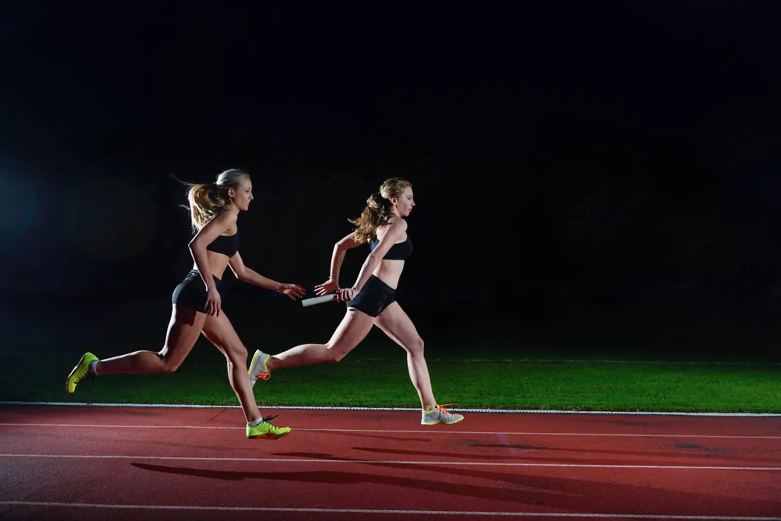 woman athletic runners passing baton in relay race.jpeg