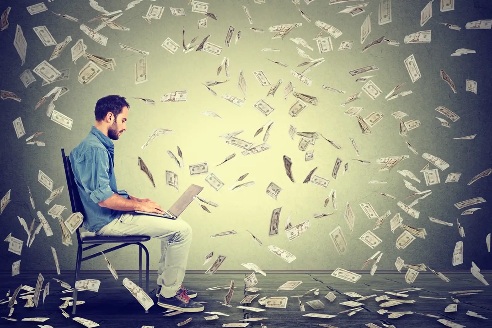 Young man using a laptop building online business making dollar bills cash falling down. Beginner IT entrepreneur under money rain. Success economy concept-1.jpeg