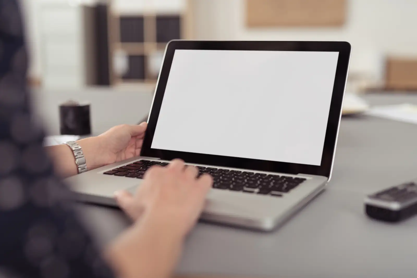 Businesswoman sitting at her desk navigating the internet on a laptop computer using the trackpad%2c over the shoulder view of the blank screen.jpeg