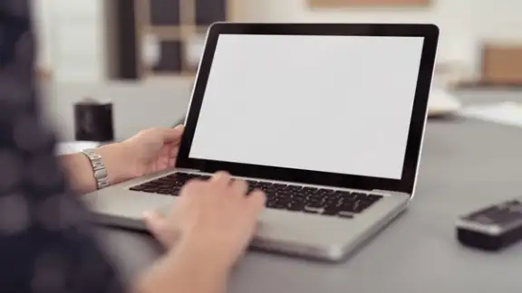 Businesswoman sitting at her desk navigating the internet on a laptop computer using the trackpad%2c over the shoulder view of the blank screen.jpeg