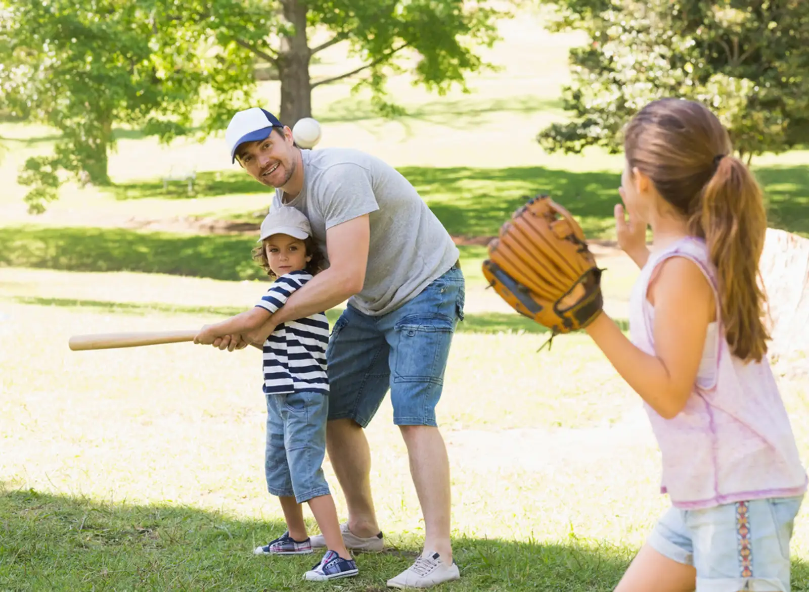 Family of three playing baseball in the park.jpeg