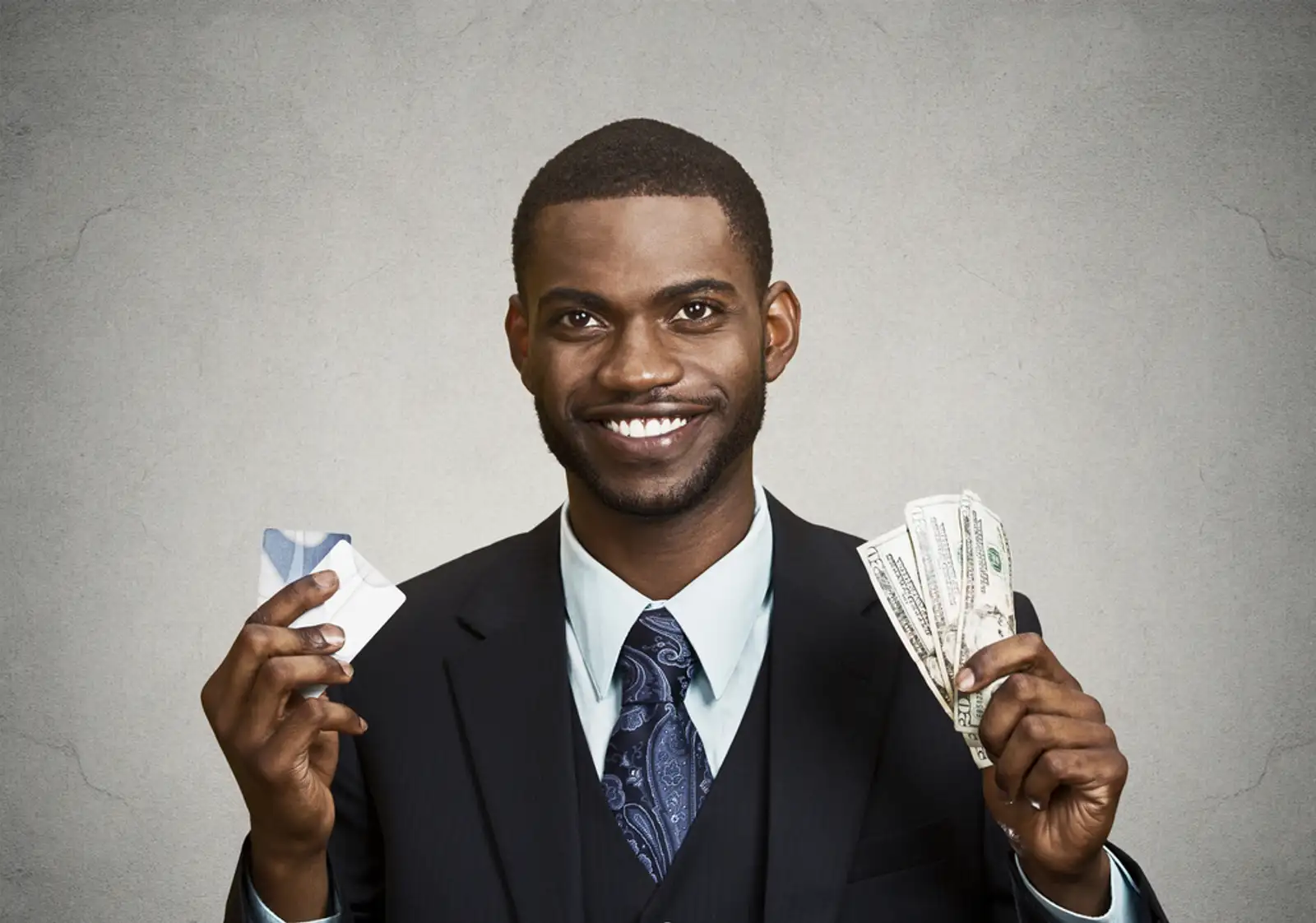 Closeup portrait happy%2c smiling business man company employee standing%2c holding dollar bills%2c credit card hand isolated grey black background. Banking exchange rate concept. Facial expression reaction.jpeg