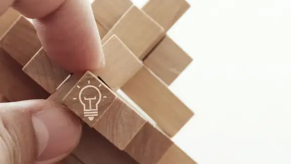 close up of hand showing illuminated light bulb icon on a wooden block puzzle as innovation concept.jpeg