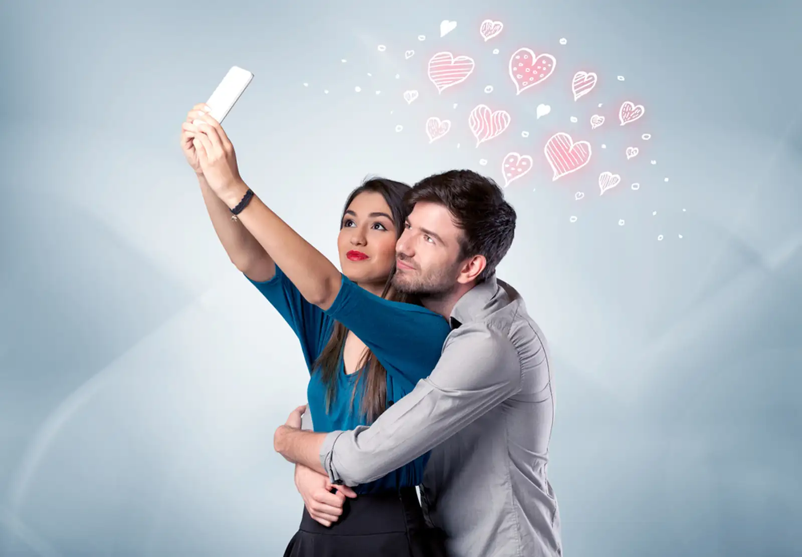 A young couple in love and drawn red hearts taking selfie with a mobile phone in the handsome guys hand in front of an empty clear grey wall background concept.jpeg