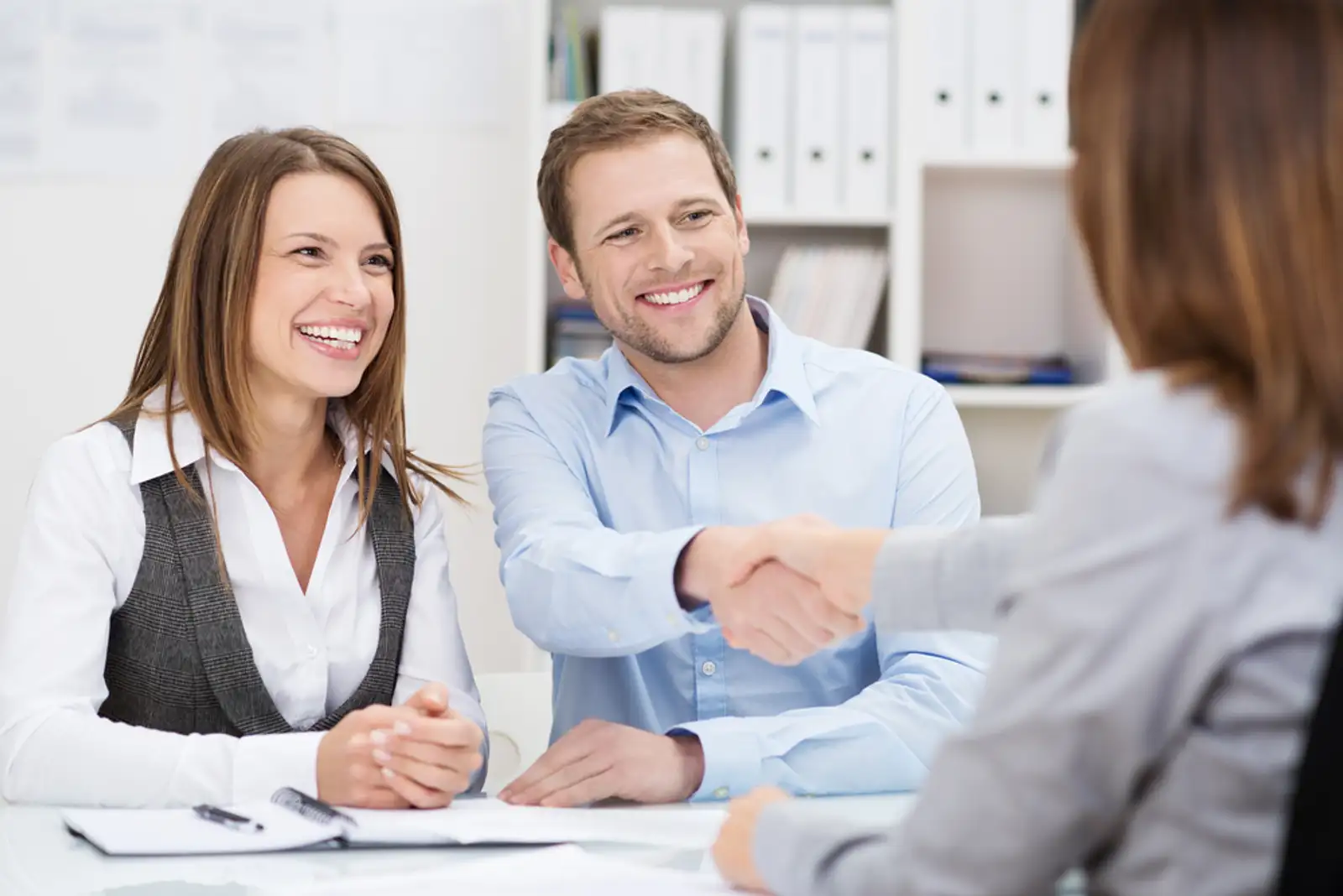 Smiling young man shaking hands with an insurance agent or investment adviser as he sits in a meeting with his wife in her office.jpeg
