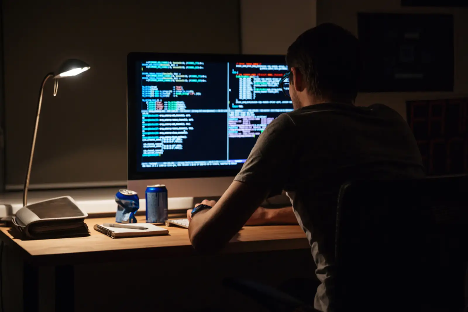 Back view of modern programmer sitting and writing code in dark room.jpeg